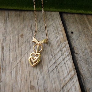 May include: A gold necklace with a pendant featuring two interlocking hearts. The hearts are open and have a delicate design.