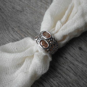 K&ouml;nnte beinhalten: Ein silberner Ring mit einem filigranen Design und zwei ovalen, orangefarbenen Edelsteinen.