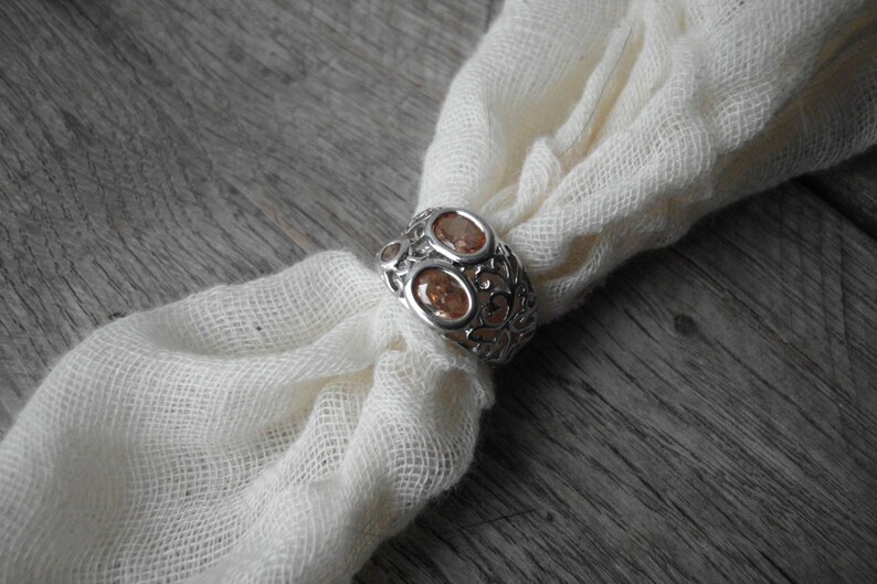 K&ouml;nnte beinhalten: Ein silberner Ring mit einem filigranen Design und zwei ovalen, orangefarbenen Edelsteinen.