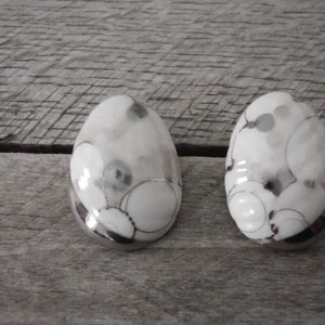 May include: Two white ceramic egg-shaped ornaments with a silver and black abstract pattern.