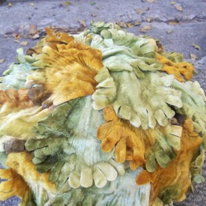 May include: A round, decorative object made of fabric with a textured, leafy design. The fabric is a mix of green, yellow, and brown colors.