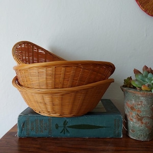 May include: Three woven wicker baskets stacked on top of each other. The baskets are oval shaped and made of natural brown wicker.