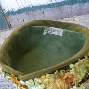 May include: A green velvet hat with a label that reads "Jacqueline II, Designed by Sally Victor". The hat is decorated with velvet leaves in shades of green, yellow, and orange.