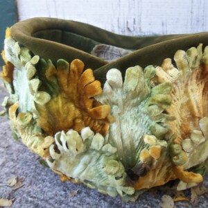 May include: A green velvet hat with a unique design featuring yellow and green velvet flowers. The hat is handmade and has a vintage look.