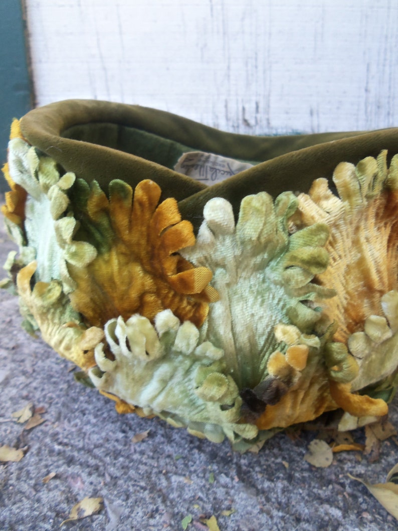 May include: A green velvet hat with a unique design featuring yellow and green velvet flowers. The hat is handmade and has a vintage look.