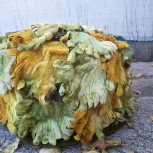 May include: A green and yellow velvet hat with a unique design. The hat is made of fabric that looks like leaves.