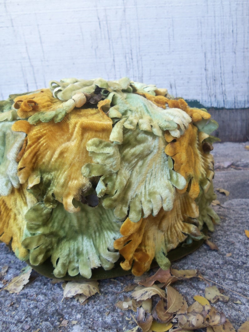 May include: A green and yellow velvet hat with a unique design. The hat is made of fabric that looks like leaves.