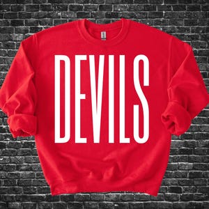 Puede incluir: Una sudadera roja con la palabra "DEVILS" impresa en letras mayúsculas blancas grandes. La sudadera tiene mangas largas y cuello redondo. El fondo es una pared de ladrillos oscuros.