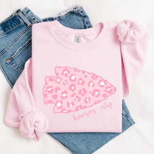 May include: Pink sweatshirt with a pink and white leopard print arrow design and the text "kansas city" in white.