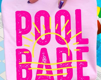 May include: A light pink t-shirt with the words "POOL BABE" in bright pink, with a yellow sun graphic. The shirt is held up by a person's hand, with a pool and a beach ball in the background.