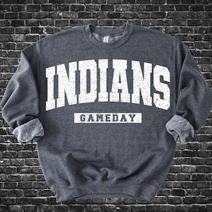 Puede incluir: Sudadera gris oscuro con la palabra "INDIANS" en letras blancas grandes en el pecho. Debajo, la palabra "GAMEDAY" se muestra en letras blancas más pequeñas. La sudadera tiene mangas con puños.