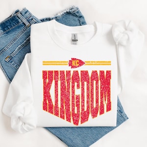 May include: White sweatshirt with a red and yellow graphic that says "KINGDOM" with a red arrowhead logo above the text.