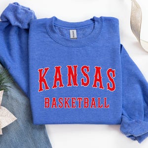 Pode incluir: Uma camisa de moletom azul com as palavras "Kansas Basketball" em letras vermelhas.