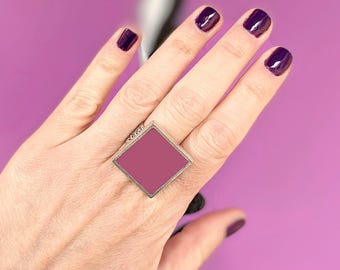 May include: A silver ring with a square, pink stone. The ring is on a person's finger.