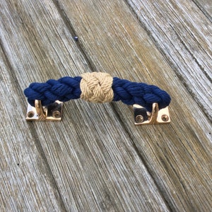 May include: A navy blue and tan rope door handle with brass hardware. The rope is braided and has a knot in the center.
