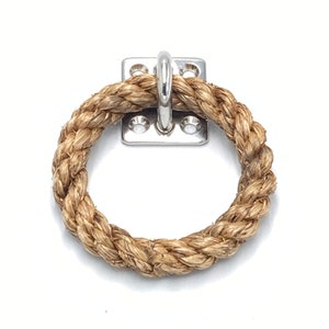 Puede incluir: Un primer plano de un anillo de cuerda natural unido a un gancho de metal plateado. El gancho está montado en una placa de metal cuadrada con cuatro agujeros.