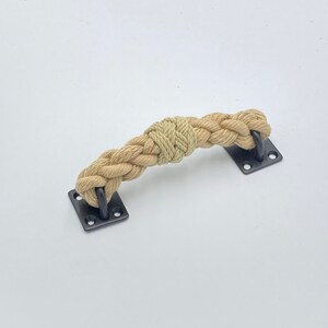 May include: A natural rope door handle with black metal hardware. The rope is braided and has a knot in the center. The handle is mounted on a white background.