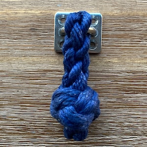 May include: A close-up of a blue rope tied to a metal plate with four holes. The rope is knotted at the end.