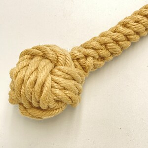 May include: A close-up of a knotted rope toy for dogs. The rope is made of natural fibers and is a light brown color. The knot is tightly woven and is a good size for a dog to chew on.