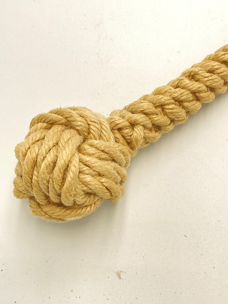 May include: A close-up of a knotted rope toy for dogs. The rope is made of natural fibers and is a light brown color. The knot is tightly woven and is a good size for a dog to chew on.