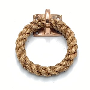 May include: Bronze-coloured metal pull with a rope handle. The metal base is square with four screw holes. The rope is thick and woven, forming a circular handle. Suitable for nautical or rustic design schemes.