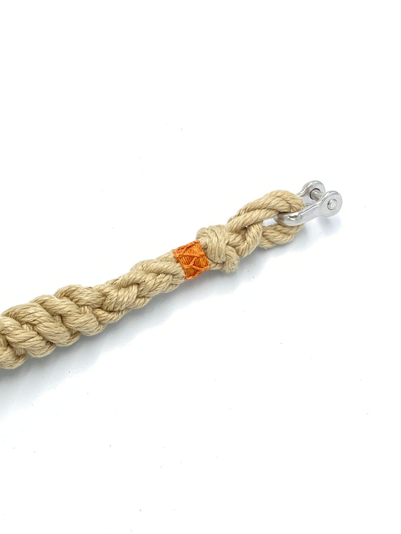 May include: A beige braided rope with an orange accent and a silver metal swivel snap hook.
