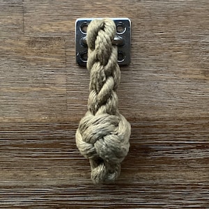 May include: A close-up of a knotted rope handle with a metal plate. The rope is a light brown color and the metal plate has four holes.