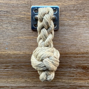 May include: A beige rope handle with a knot at the end, attached to a silver metal plate with four holes.