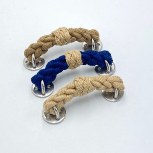 May include: Three rope cabinet pulls with a knotted design. Two are natural colored rope and one is blue rope. Each pull has a silver metal ring on each end.