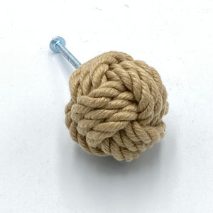 Peut inclure: Un bouton en corde beige avec une vis argentée. La corde est nouée en forme de sphère.