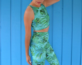 May include: A woman wearing a green and blue tropical print crop top and leggings. The outfit has a high waisted design. She is wearing white sneakers.