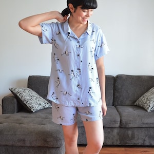 May include: A light blue pajama set with a short-sleeved button-up shirt and matching shorts. The shirt and shorts feature a pattern of black and white birds.