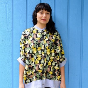 Può includere: Una donna indossa una camicia abbottonata con stampa floreale bianco e nero con bordino grigio e leggings neri con logo Adidas bianco.