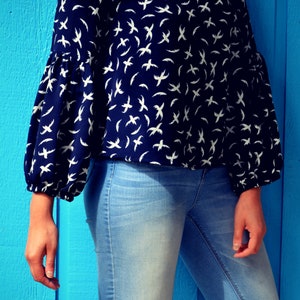 May include: A woman is wearing a blue blouse with a white bird print and blue jeans. The blouse has long sleeves and a loose fit.