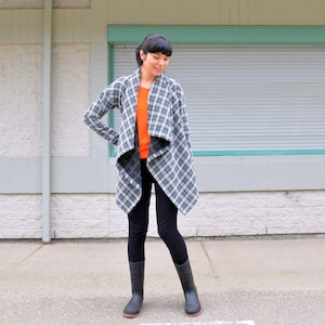 Pode incluir: Uma mulher vestindo um cardigã de envoltório xadrez preto e branco com uma camisa de manga comprida preta e laranja por baixo. Ela está vestindo calças pretas e botas pretas.