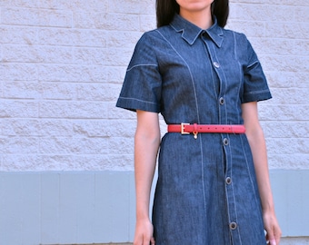 May include: A denim shirt dress with a collared neckline and short sleeves. The dress has a red belt with a gold buckle.