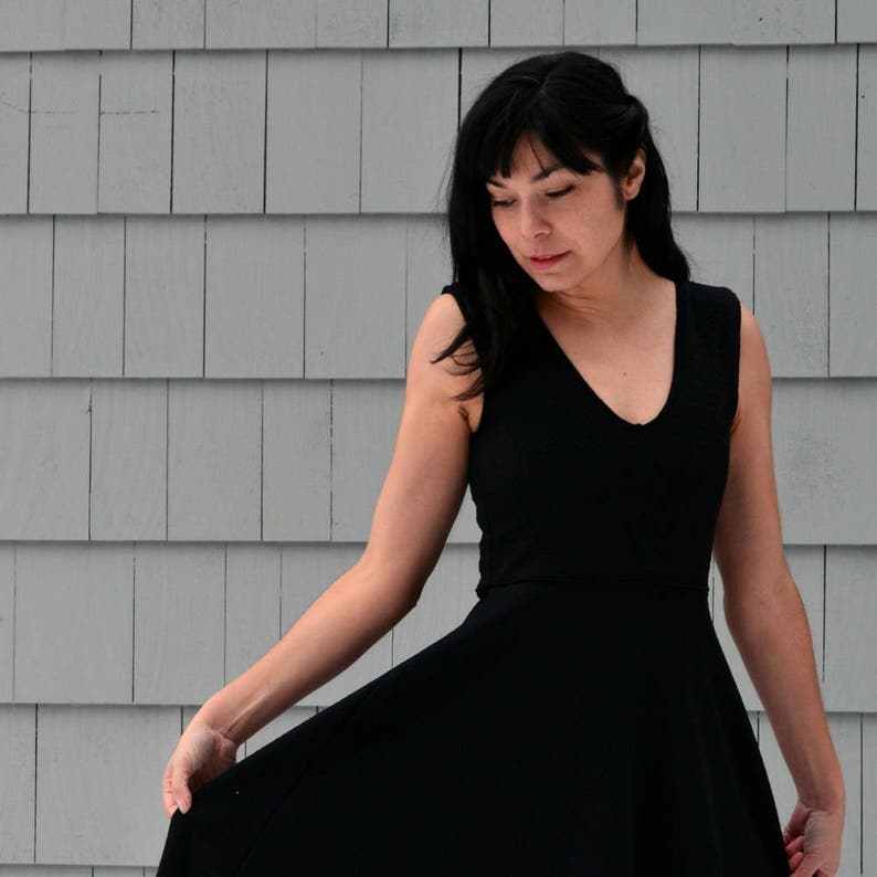 Pode incluir: Uma mulher vestindo um vestido preto sem mangas com decote em V. O vestido tem uma saia rodada e &eacute; ajustado na cintura.