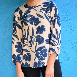 May include: A cream-colored blouse with a blue floral print. The blouse has a round neckline and long sleeves.