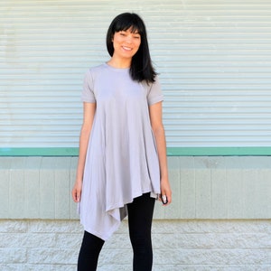 May include: A woman wearing a light grey, asymmetrical tunic top with short sleeves and black leggings.