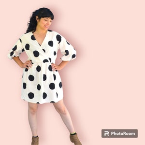 Peut inclure: Une robe blanche à pois noirs et un col en V enveloppant. La robe a des manches 3/4 et une longueur courte.