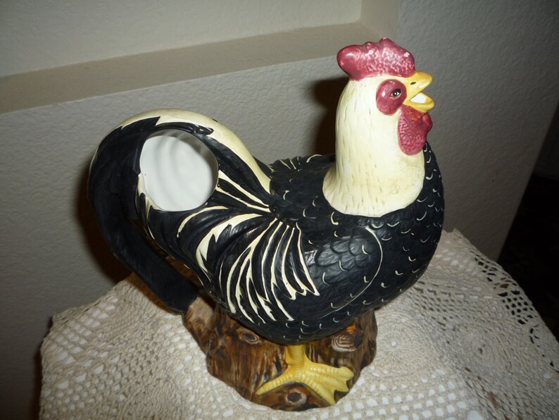 Peut inclure: Figurine de coq noir et blanc avec une cr&ecirc;te et des barbillons rouges. Le coq est debout sur une souche d'arbre brune. La figurine est en c&eacute;ramique et a un trou dans le dos pour servir de vase.
