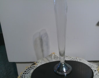 May include: A clear glass vase with a silver base. The vase is tall and slender, with a round base. The vase is sitting on a black surface.