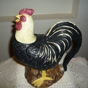 Peut inclure: Une figurine de coq noir et blanc avec une cr&ecirc;te et des barbillons rouges. Le coq est debout sur une souche d'arbre brune. La figurine est en c&eacute;ramique et a une finition brillante.