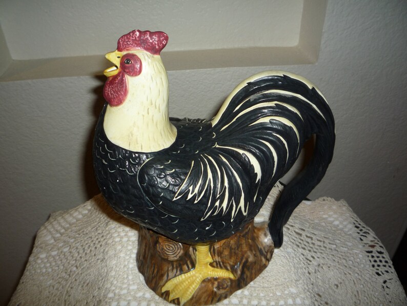 Peut inclure: Une figurine de coq noir et blanc avec une cr&ecirc;te et des barbillons rouges. Le coq est debout sur une souche d'arbre brune. La figurine est en c&eacute;ramique et a une finition brillante.