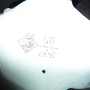 May include: A white porcelain figurine with a Nao logo and the text "Hand made in Spain by Lladro&reg; &copy; Lladro SA 1989".