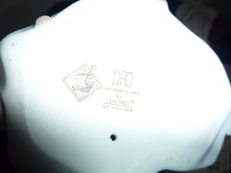 May include: A white porcelain figurine with a Nao logo and the text "Hand made in Spain by Lladro&reg; &copy; Lladro SA 1989".