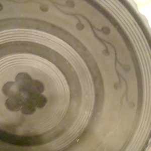 May include: A close-up of a ceramic plate with a concentric circle design and a floral pattern. The plate is a light brown color with darker brown accents.