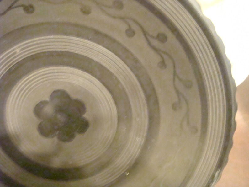 May include: A close-up of a ceramic plate with a concentric circle design and a floral pattern. The plate is a light brown color with darker brown accents.