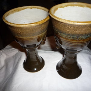 May include: Two brown ceramic goblets with a white glaze inside. The goblets have a wide base and a rounded bowl.