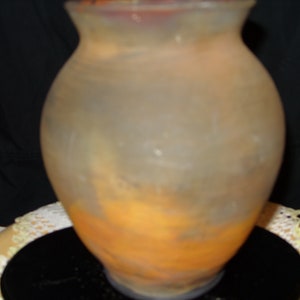 May include: A frosted glass vase with a swirling orange and yellow design. The vase is clear and has a textured surface.
